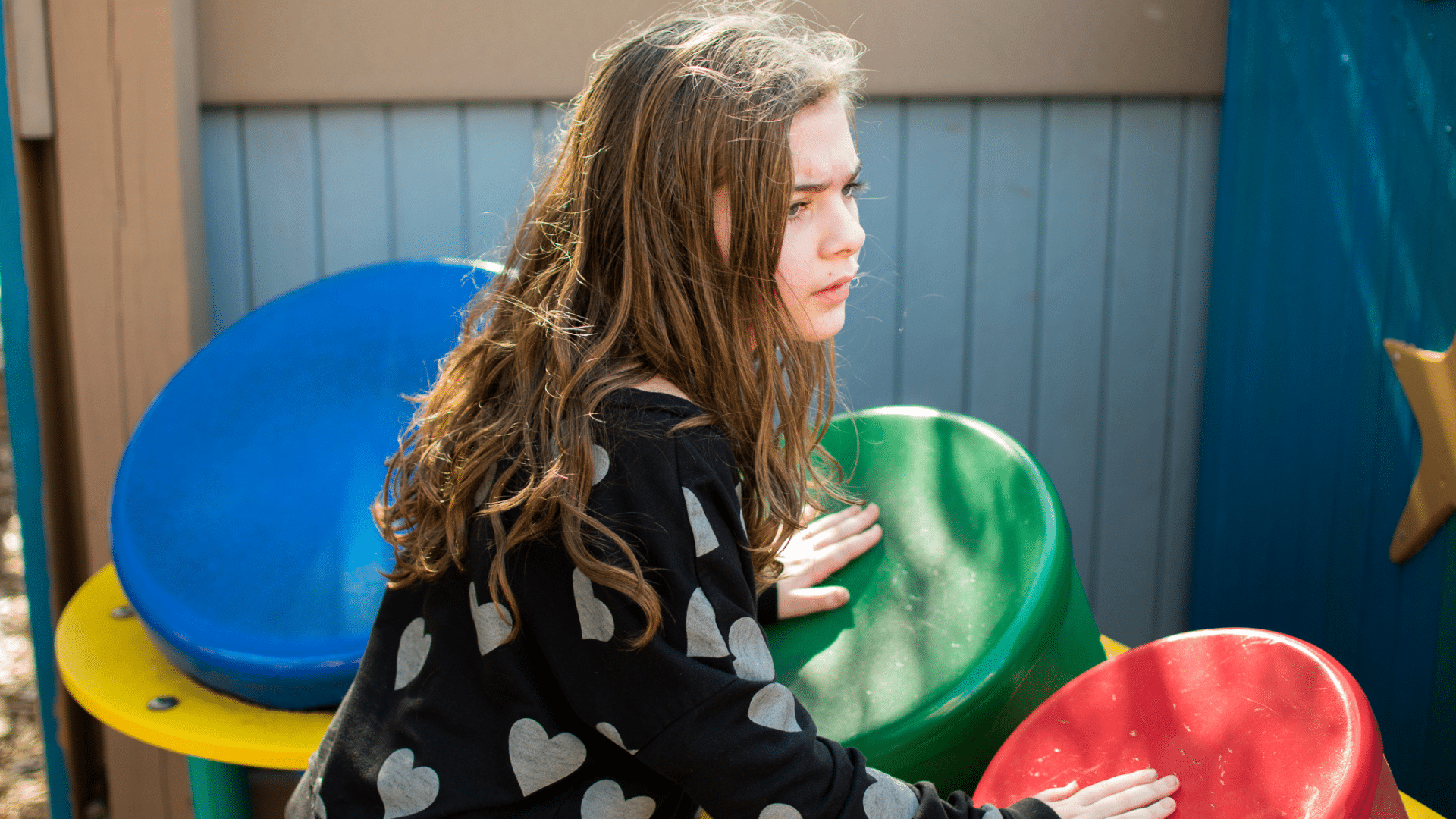 a girl with long hair and a black shirt with white hearts on it playing drums at Perdido Kids Park